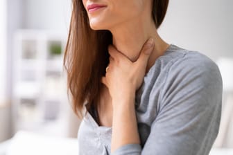 Frau fasst sich an den Hals: In manchen Fällen kommt ein Kloß im Hals von einer vergrößerten Schilddrüse.