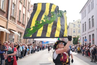 Fahnenschwinger schreiten beim Festumzug zum Tag der Sachsen durch das Stadtzentrum von Aue-Bad Schlema: