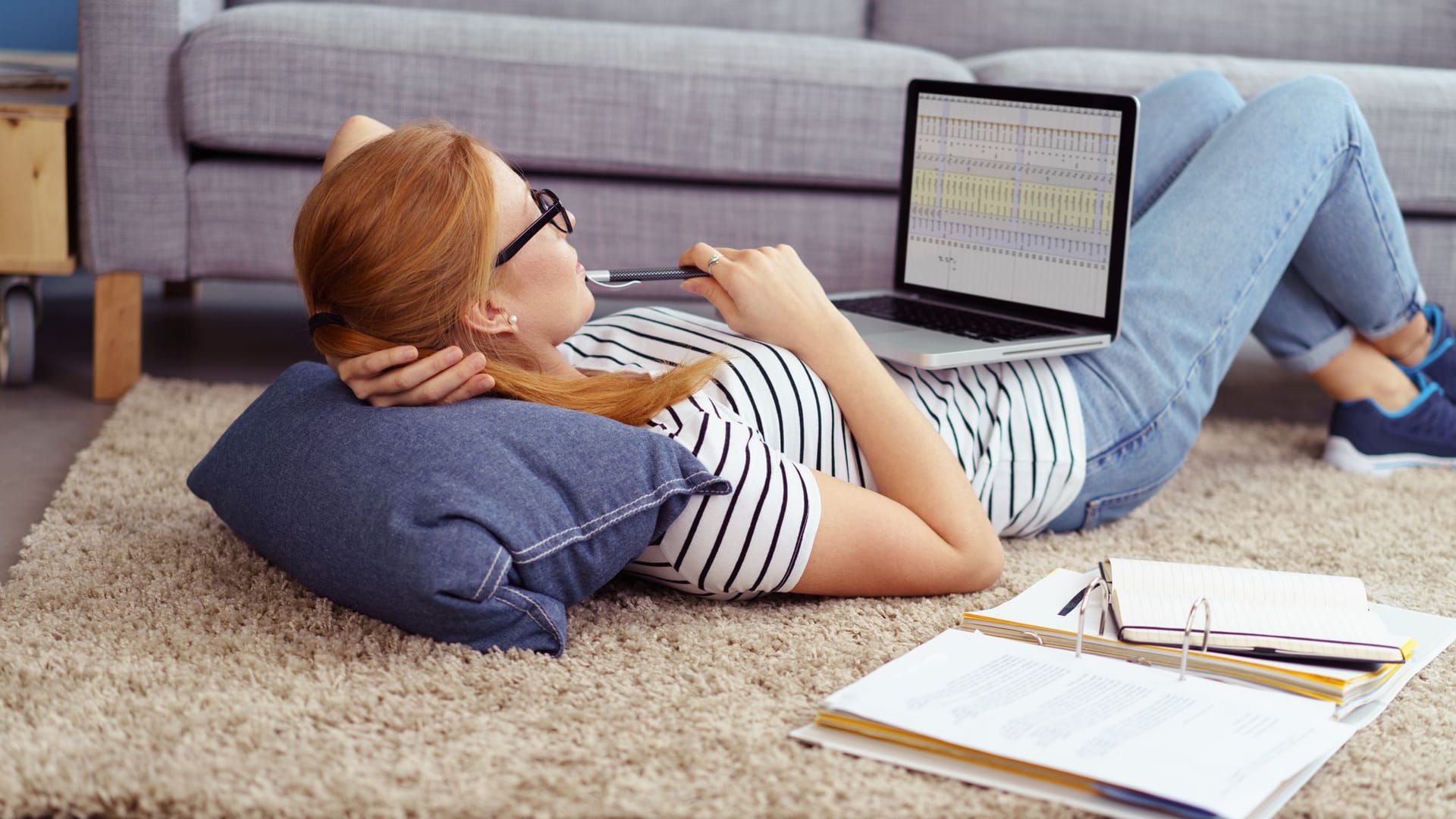 Junge Frau arbeitet liegend am Laptop: Aktienhandel funktioniert heute deutlich einfacher als vor 30 Jahren.