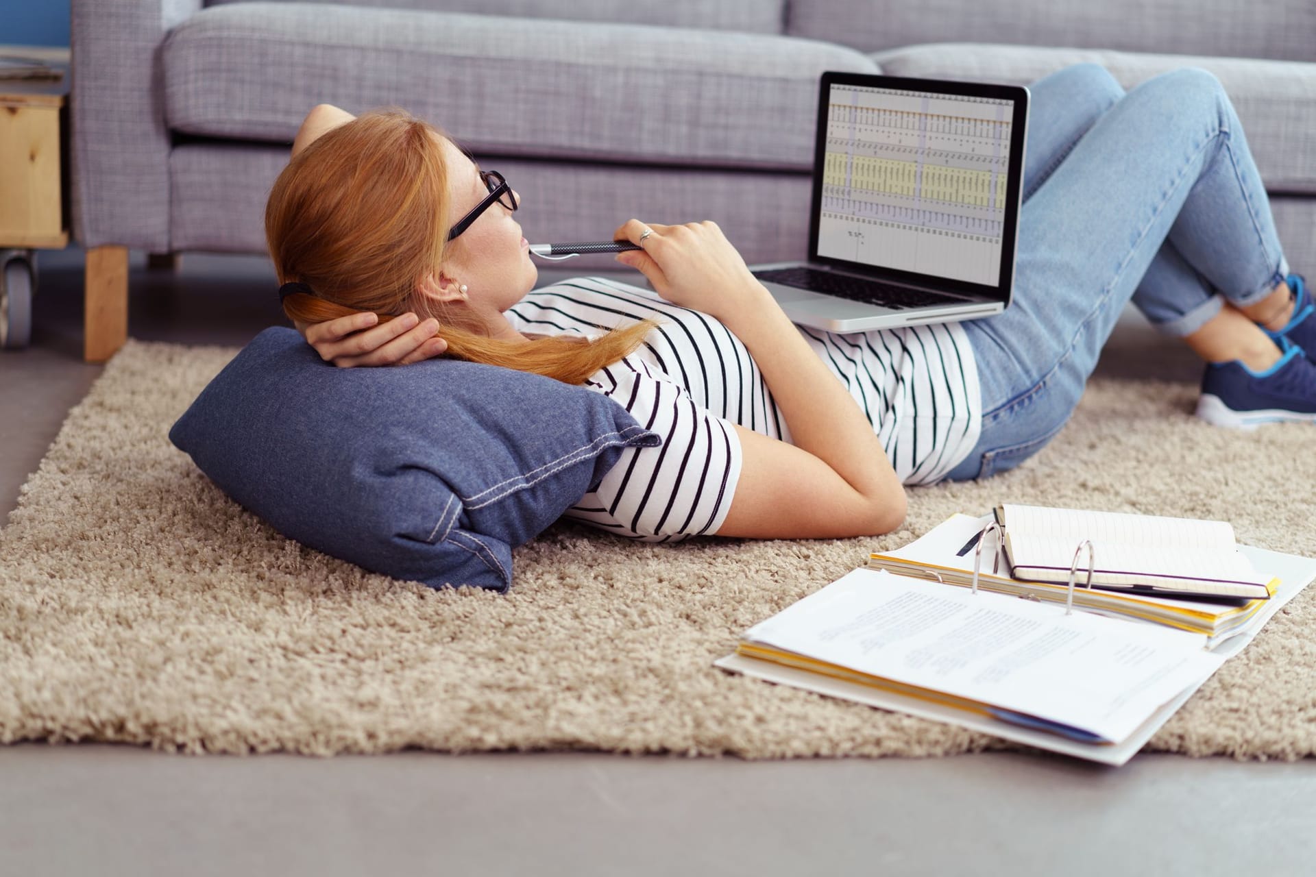 Junge Frau arbeitet liegend am Laptop: Aktienhandel funktioniert heute deutlich einfacher als vor 30 Jahren.