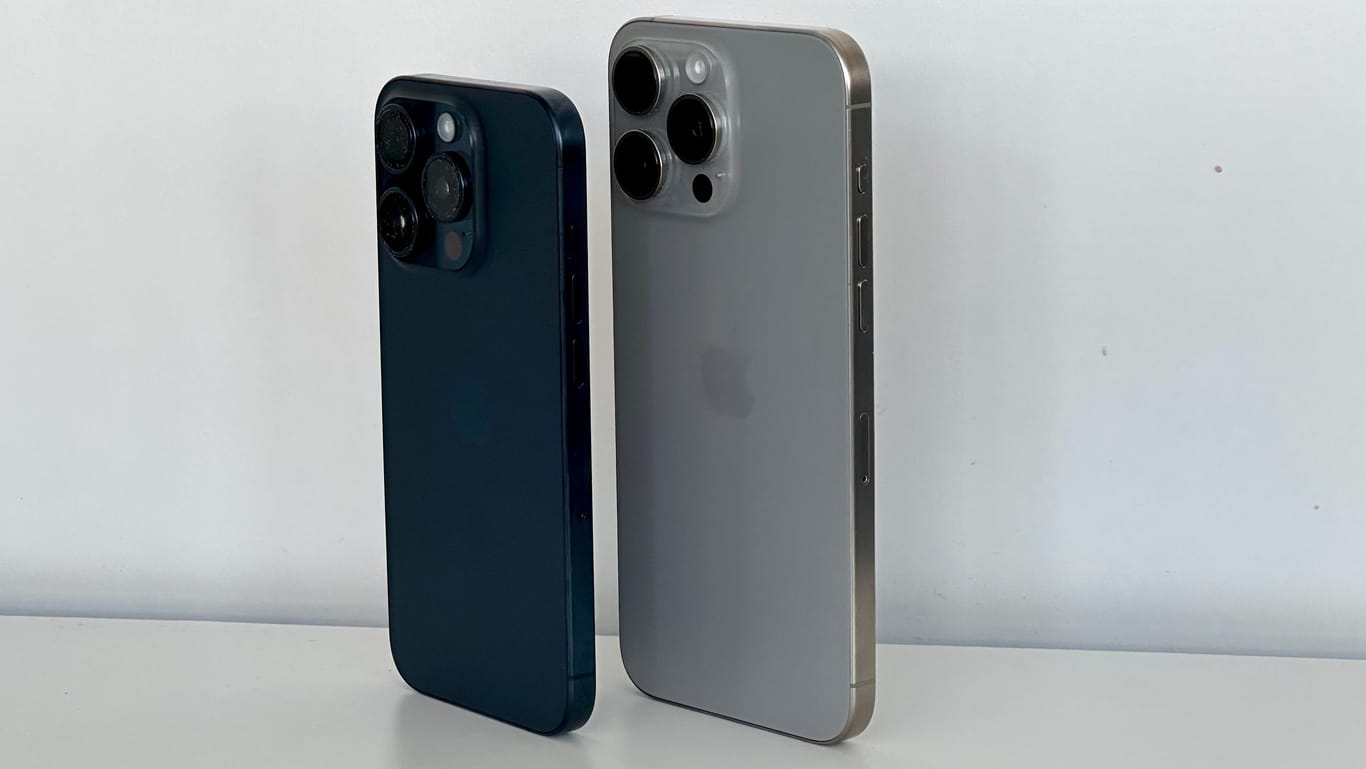 iPhone 15 Pro in Blau (links) und iPhone 15 Pro Max in Natur bei normalem Tageslicht. Das Blau wirkt oft sehr dunkel.