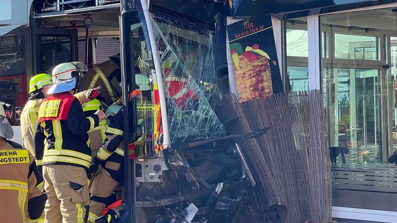 Einsatzkräfte der Feuerwehr untersuchen den beschädigten Linienbus, der in einen Dönerladen gekracht ist.