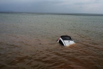 Ein Auto ist nach einem Rekordregen halb im Meer versunken: Mehrere Tote sind bereits geborgen worden, Rettungskräfte suchen weiter nach Vermissten.