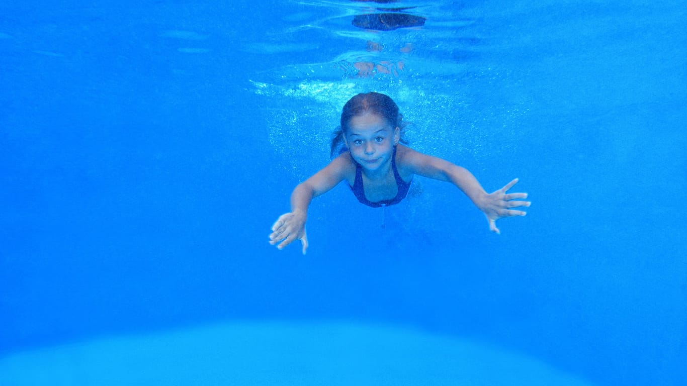 Mädchen taucht in einem Schwimmbecken und schwimmt auf die Kamera zu.