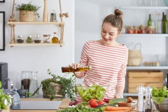 Eine Frau bereitet einen Salat mit Öl zu.