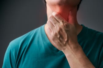 Ein Mann greift sich an den Hals: Eine refluxbedingte Speiseröhrenentzündung kann sich durch einen Kloß im Hals äußern.