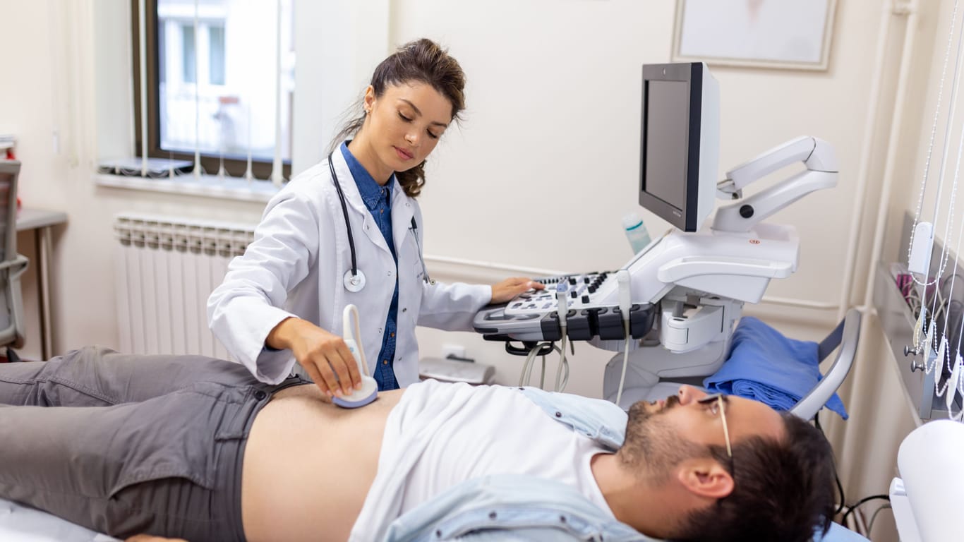 Eine Ärztin untersucht den Bauch eines Mannes mit Ultraschall.