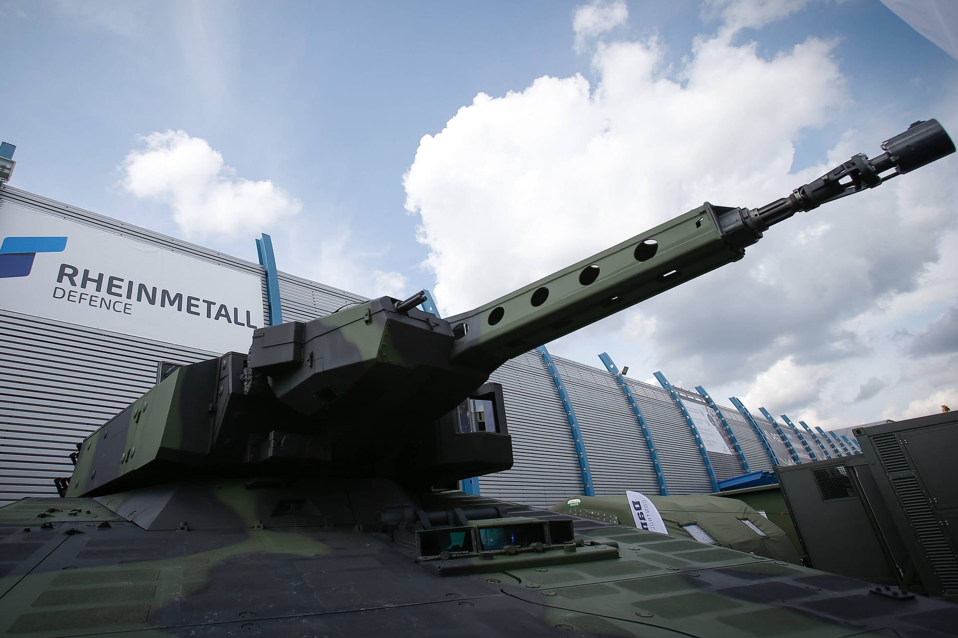 Gepanzertes Fahrzeug vor dem Logo von Rheinmetall (Symbolbild): Die Rheinmetallaktie profitiert von der Eskalation im Nahen Osten.