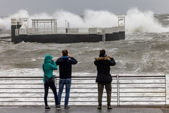 Menschen in Kiel-Schilksee fotografieren die über die Hafenanlagen niedergehenden Wellen: Der Ostseeküste droht eine Jahrhundertflut.