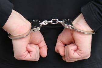 Ein Mann ist mit Handschellen gefesselt (Symbolbild): Der Verdächtige schweigt bislang zu den Vorwürfen.