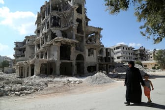 Eine Frau läuft in Homes mit ihrem Kind an einem zerstörten Gebäude vorbei (Syrien): Das Land befindet sich im Bürgerkrieg.