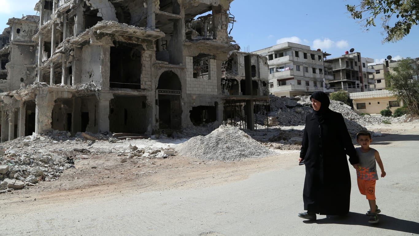 Eine Frau läuft in Homes mit ihrem Kind an einem zerstörten Gebäude vorbei (Syrien): Das Land befindet sich im Bürgerkrieg.