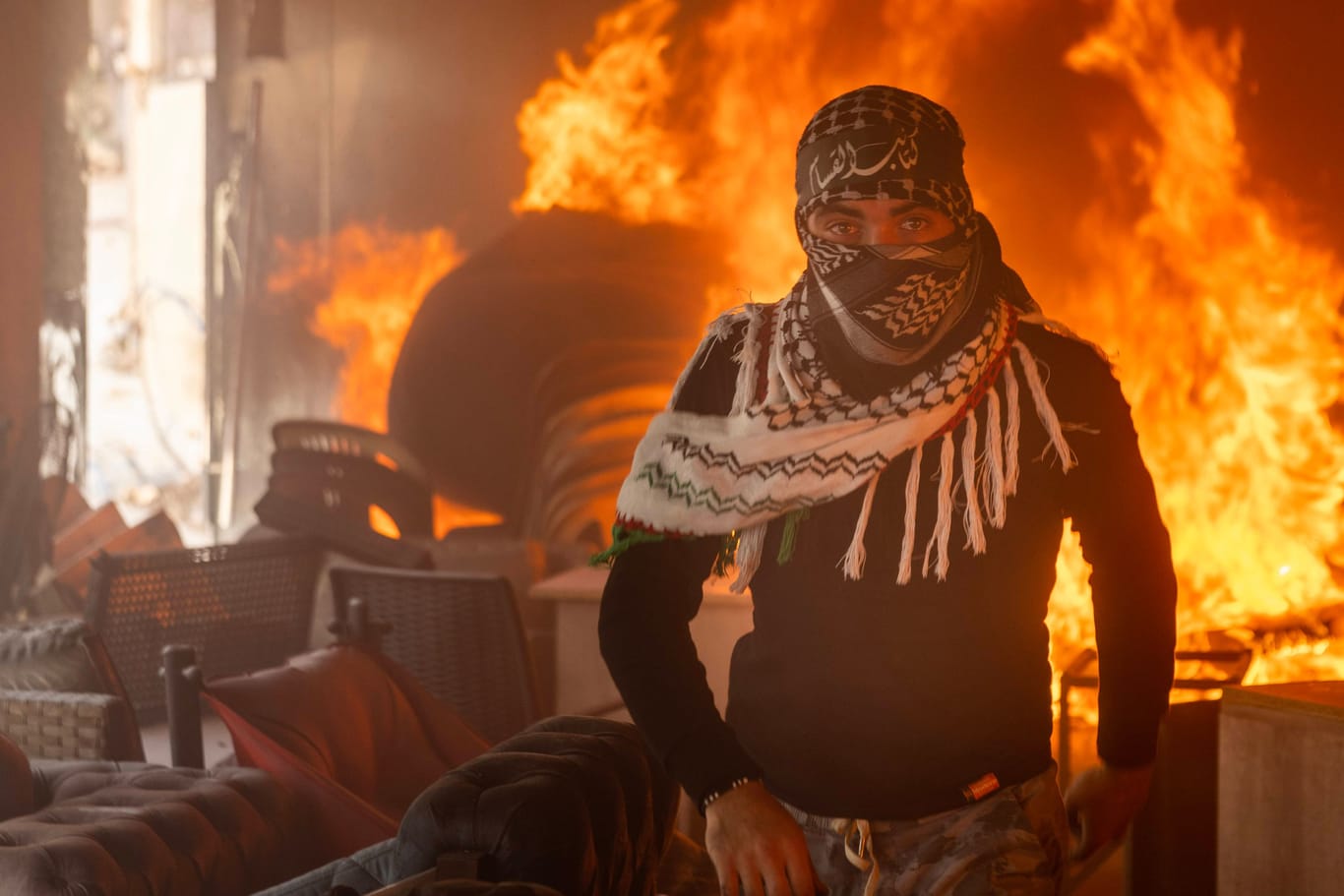 Ein vermummter Demonstrant steht vor einem brennenden Gebäude: Im Nahen und Mittleren Osten kam es bei pro-palästinensischen Demonstrationen zu massiver Gewalt gegen israelische Einrichtungen.