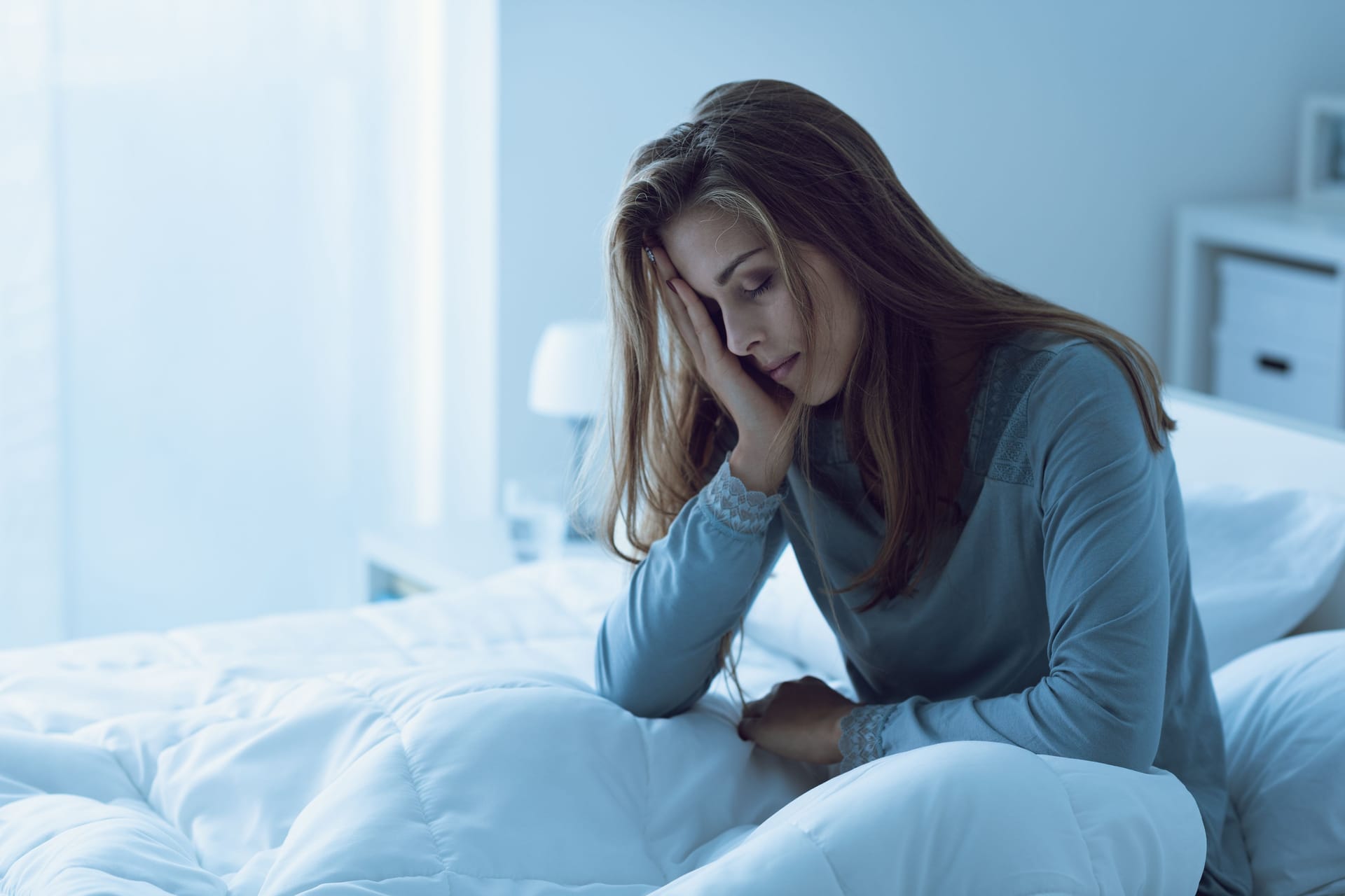 Eine Frau sitzt im Bett und fasst sich an den Kopf.