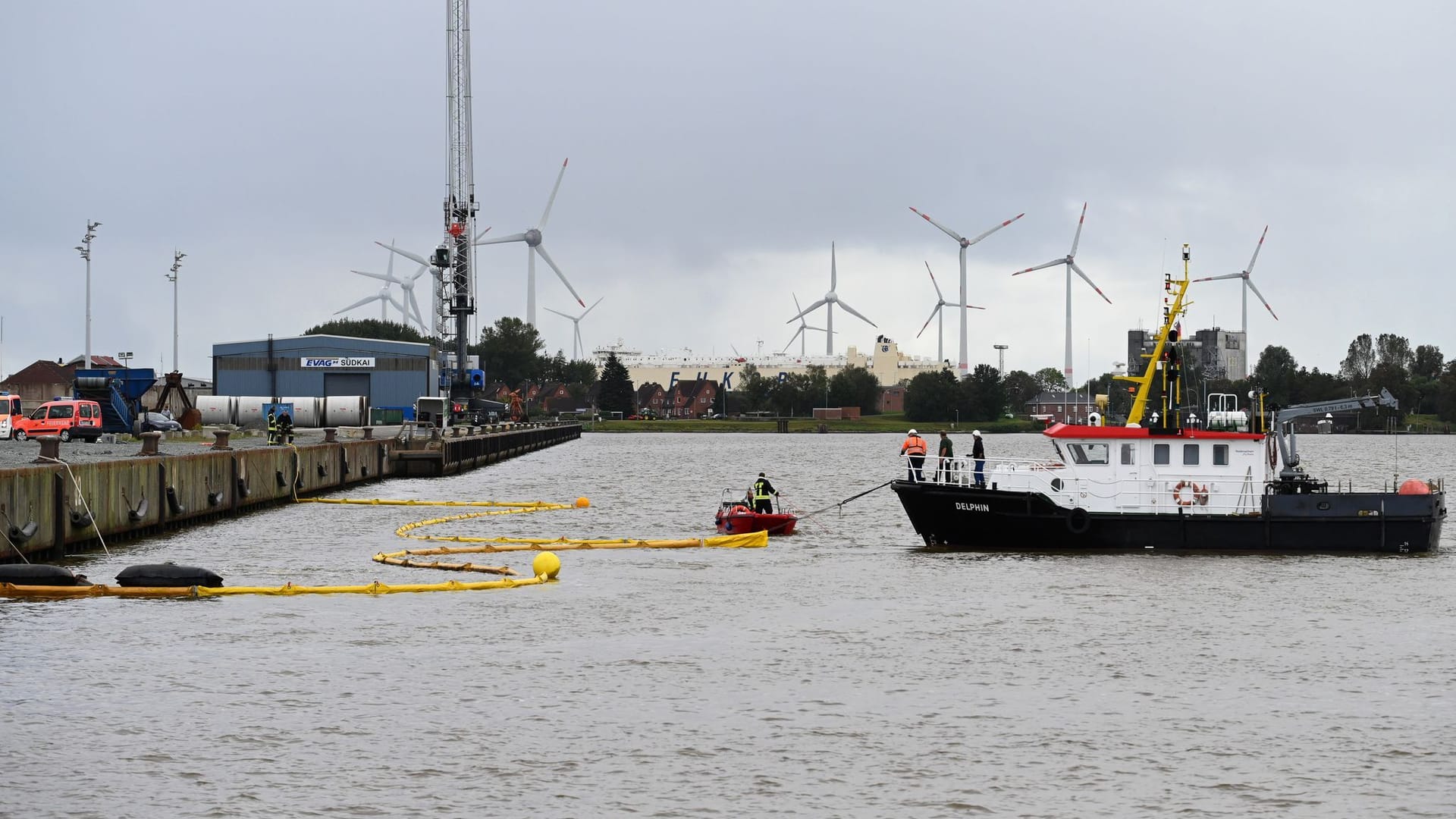 Die Feuerwehr bringt mithilfe von zwei Schiffen Ölsperren im Hafen aus.