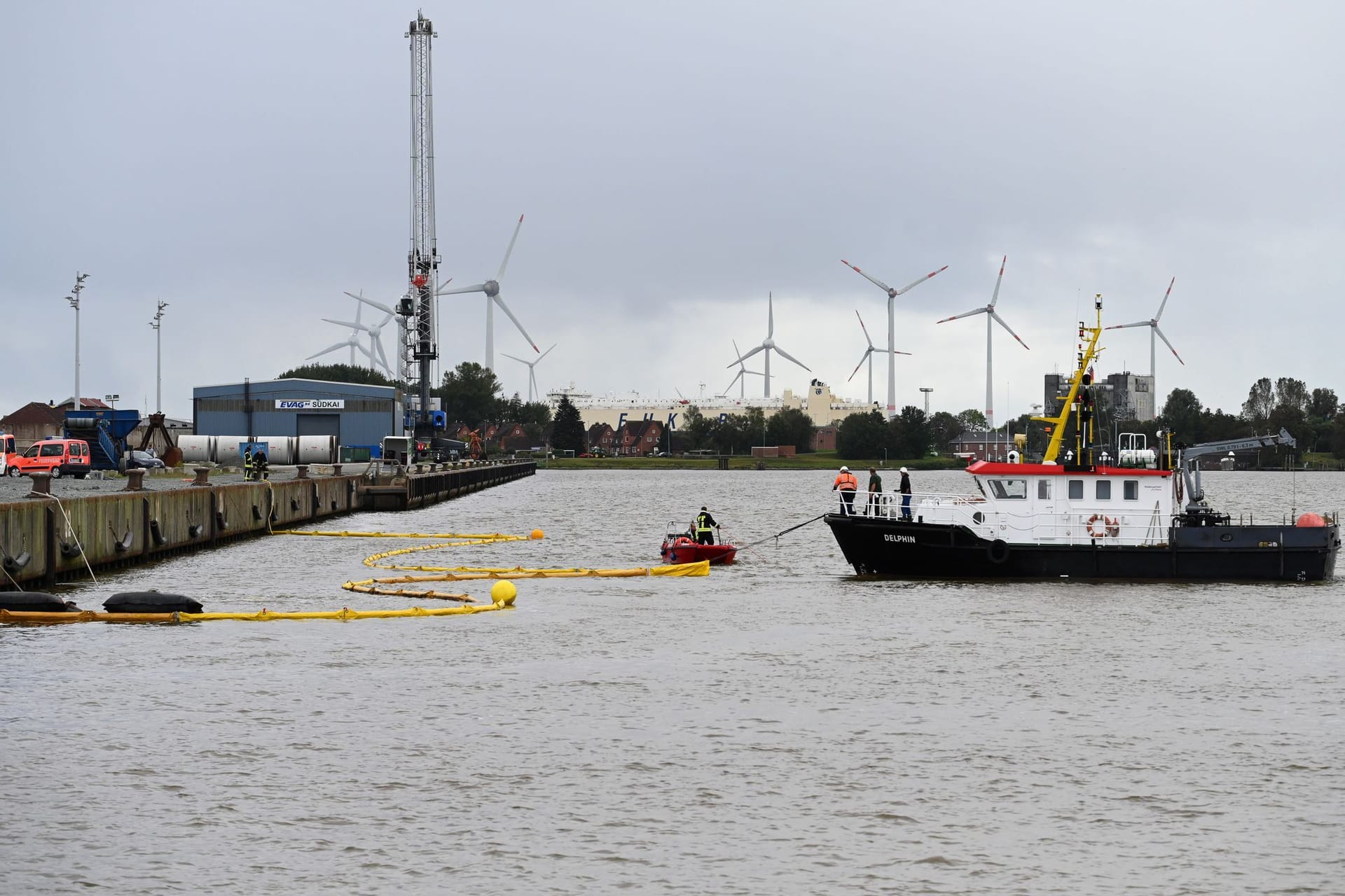 Die Feuerwehr bringt mithilfe von zwei Schiffen Ölsperren im Hafen aus.