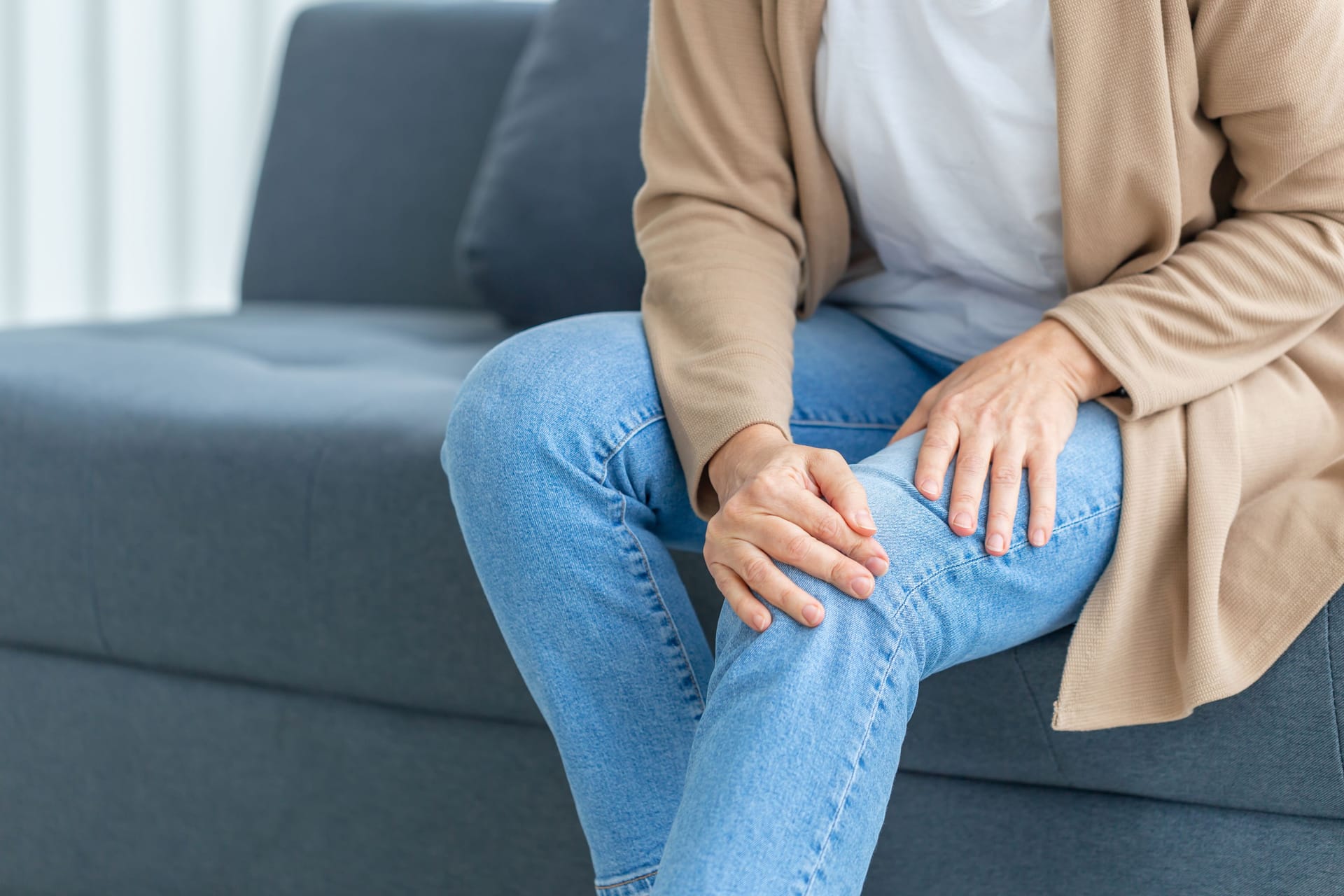 Eine Frau sitzt auf der Couch und hält sich das Bein.