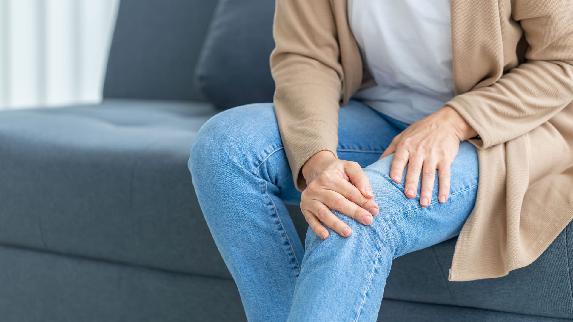 Eine Frau sitzt auf der Couch und hält sich das Bein.