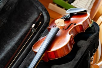 Violin, fiddle with a bow laying in an open black case on the table, small xylophone in the back. Simple classical musical string instruments group concept, nobody. Safe instrument storage for travel
