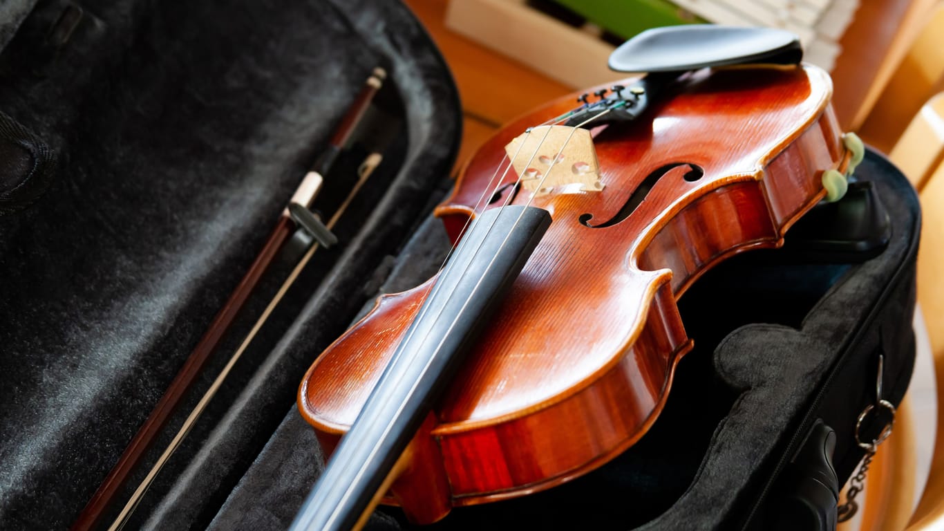 Violin, fiddle with a bow laying in an open black case on the table, small xylophone in the back. Simple classical musical string instruments group concept, nobody. Safe instrument storage for travel