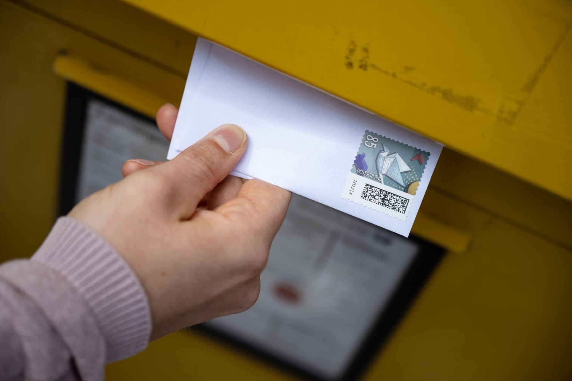 Person steckt einen Brief in einen Briefkasten Person steckt einen Brief in einen Briefkasten