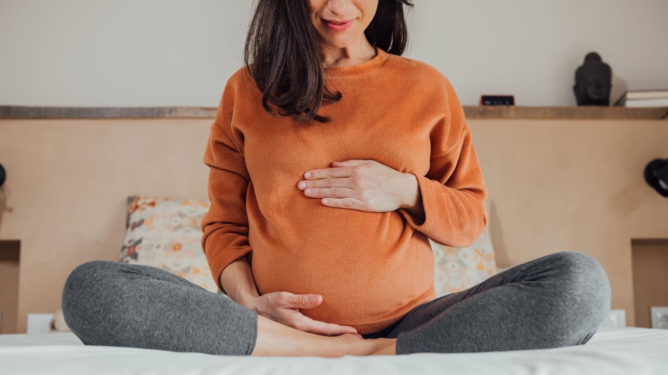 Schwangere Frau sitzt im Schneidersitz auf dem Bett: Eine ausreichende Vitamin-A-Zufuhr ist für schwangere Frauen unerlässlich – eine übermäßig hohe Zufuhr sollte hingegen vermieden werden.