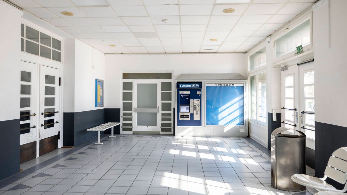 Die triste Wartehalle des Bahnhofs: Hier befinden sich ein Fahrkartenautomat, eine Bank und mehrere Stühle.