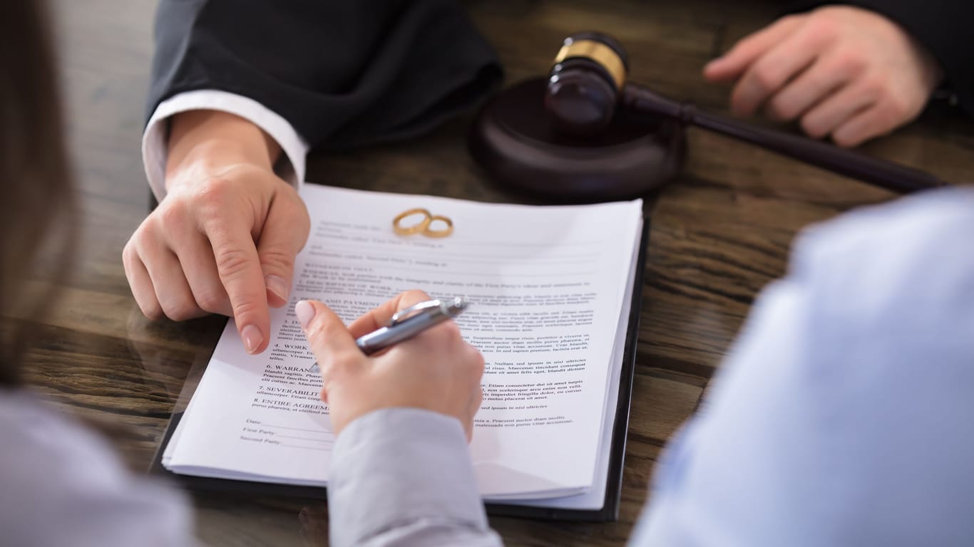 Eine Frau unterschreibt ein Dokument (Symbolbild): Beim Scheidungstermin müssen beide Partner anwesend sein.