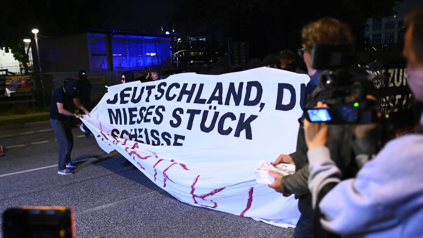 Vermummter Demonstrant enthüllt ein vulgäres Plakat auf der Hamburger Demo.