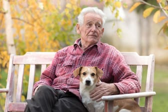 Rentner sitzt mit seinem Hund auf einer Gartenbank