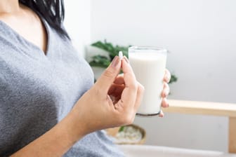 Eine Frau hält eine Tablette in der rechten und ein Glas Milch in der linken Hand: Antibiotika und Milch(-produkte) sind nicht immer eine gute Kombination.