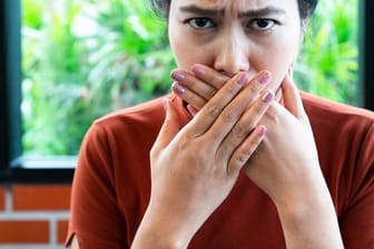 Eine Frau bedeckt ihren Mund mit den Händen: Den ein oder anderen Trick, um Schluckauf loszuwerden, kennen die meisten.