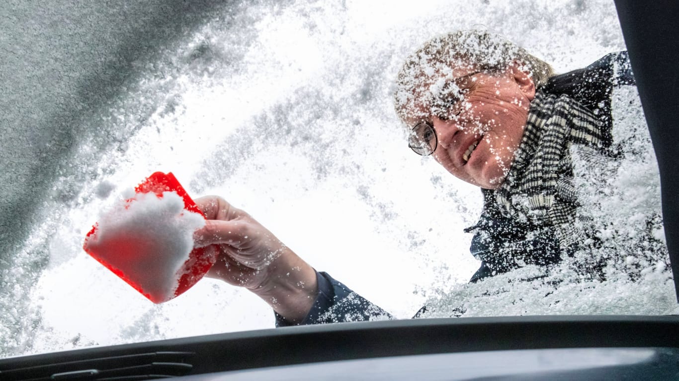 Ein Mann befreit sein Auto vom Schnee (Archivbild): In dieser Woche könnte es auch in München die ersten Flocken geben.