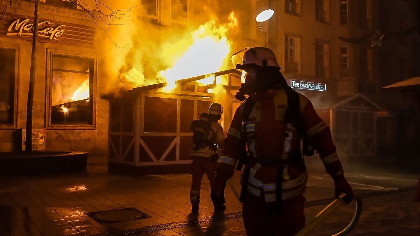 Einsatzkräfte der Feuerwehr vor der brennenden Hütte: Das Feuer auf dem Flensburger Weihnachtsmarkt konnte schnell gelöscht werden. Einsatzkräfte der Feuerwehr vor der brennenden Hütte: Das Feuer auf dem Flensburger Weihnachtsmarkt konnte schnell gelöscht werden.