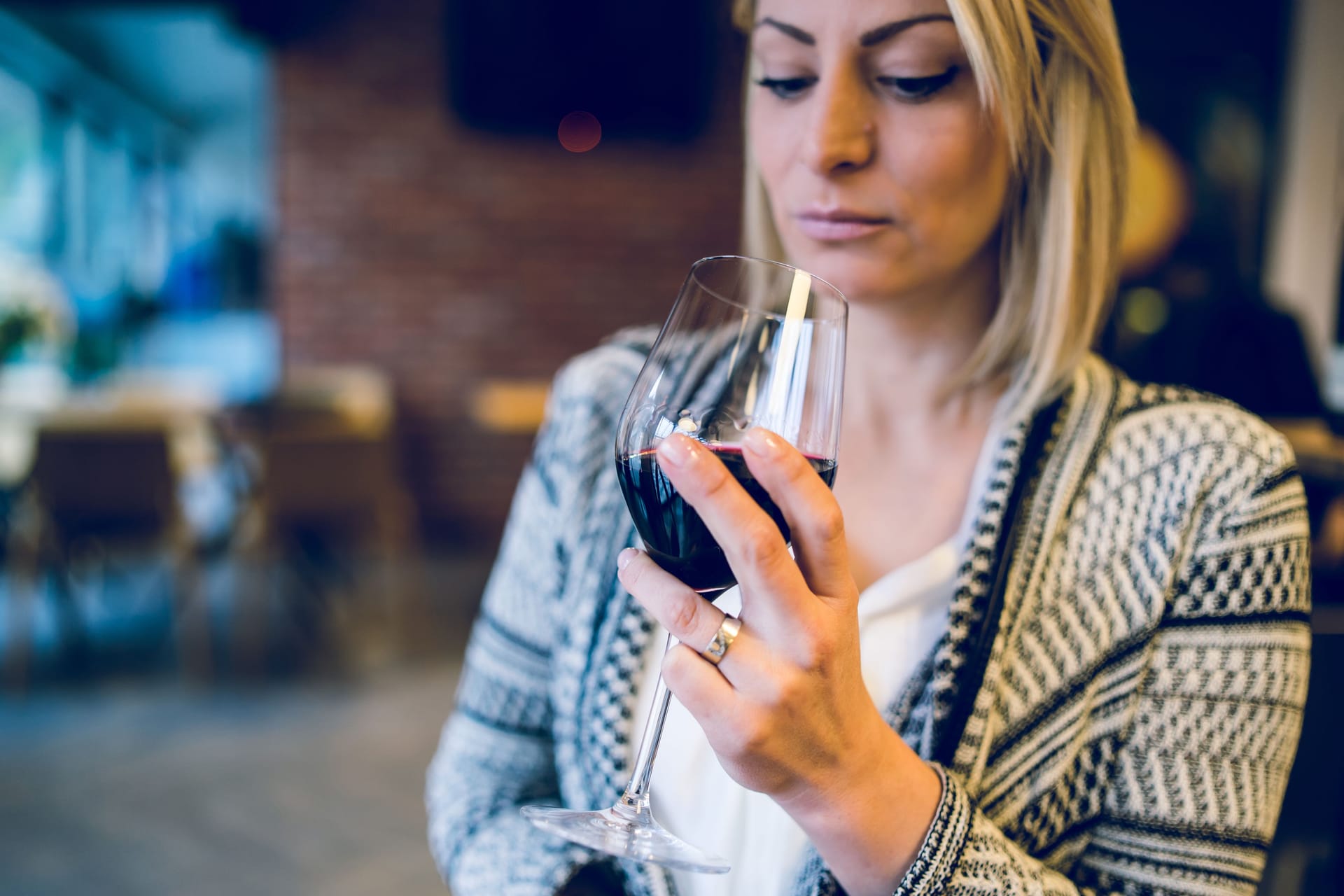 Eine Frau blickt in das Glas Rotwein in ihrer Hand.