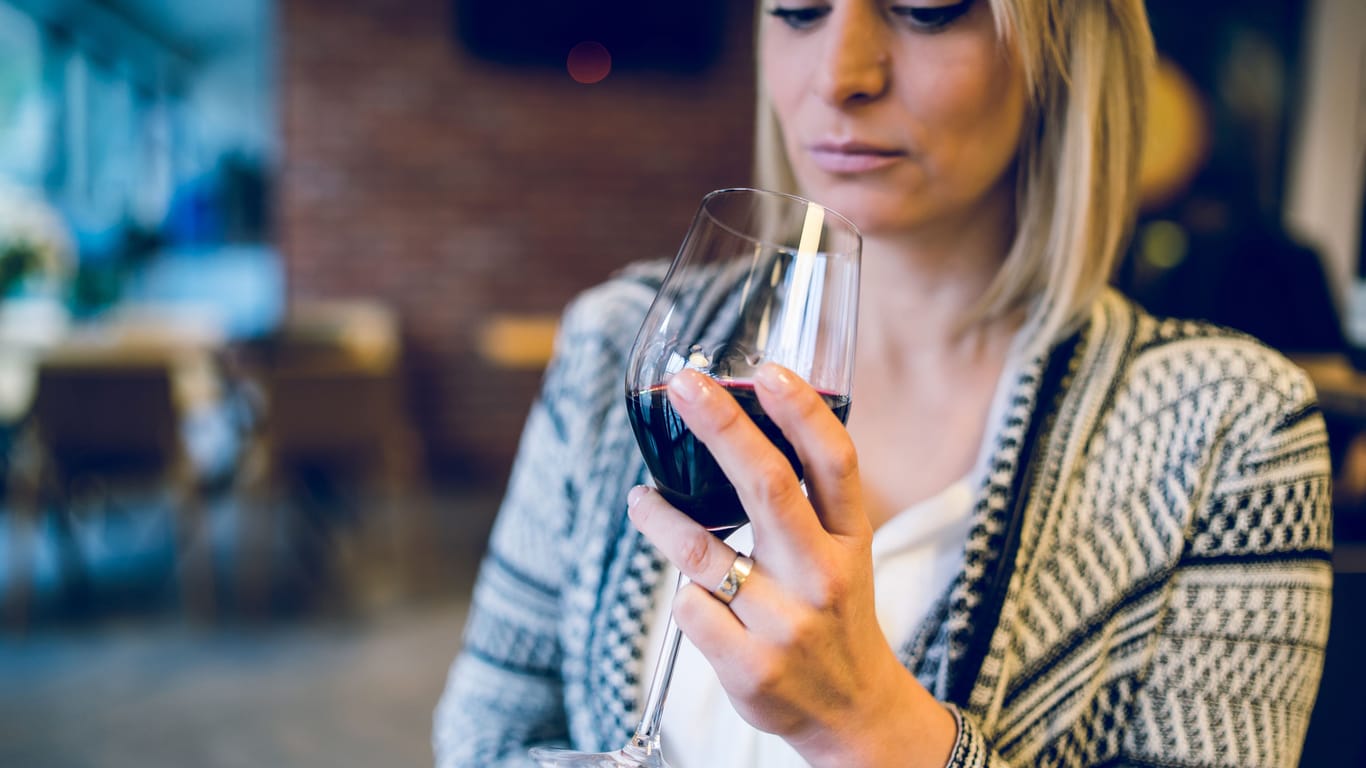 Eine Frau blickt in das Glas Rotwein in ihrer Hand.