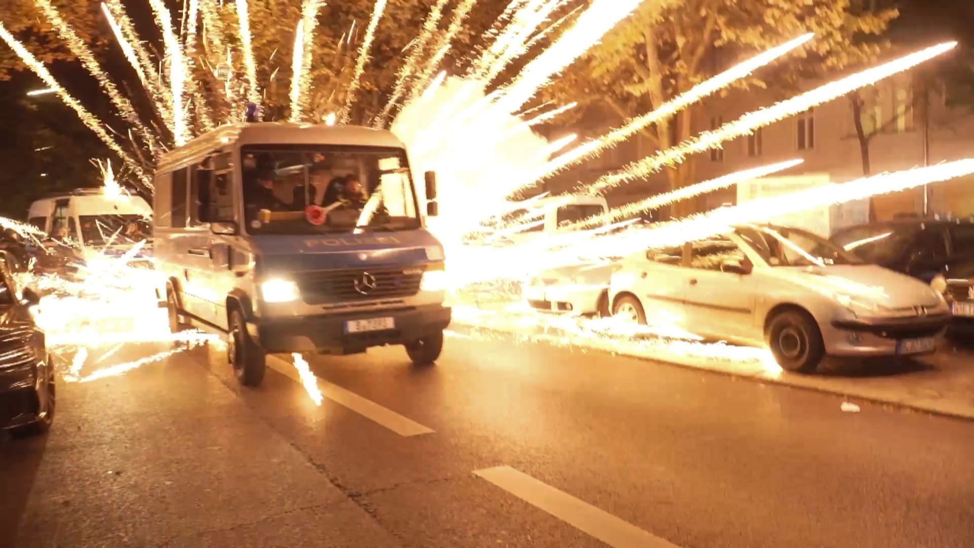 18.10.2023, Berlin: Feuerwerkskörper fliegen hinter einem Polizeiauto bei einer nicht angekündigten pro-palästinensischen Demonstration