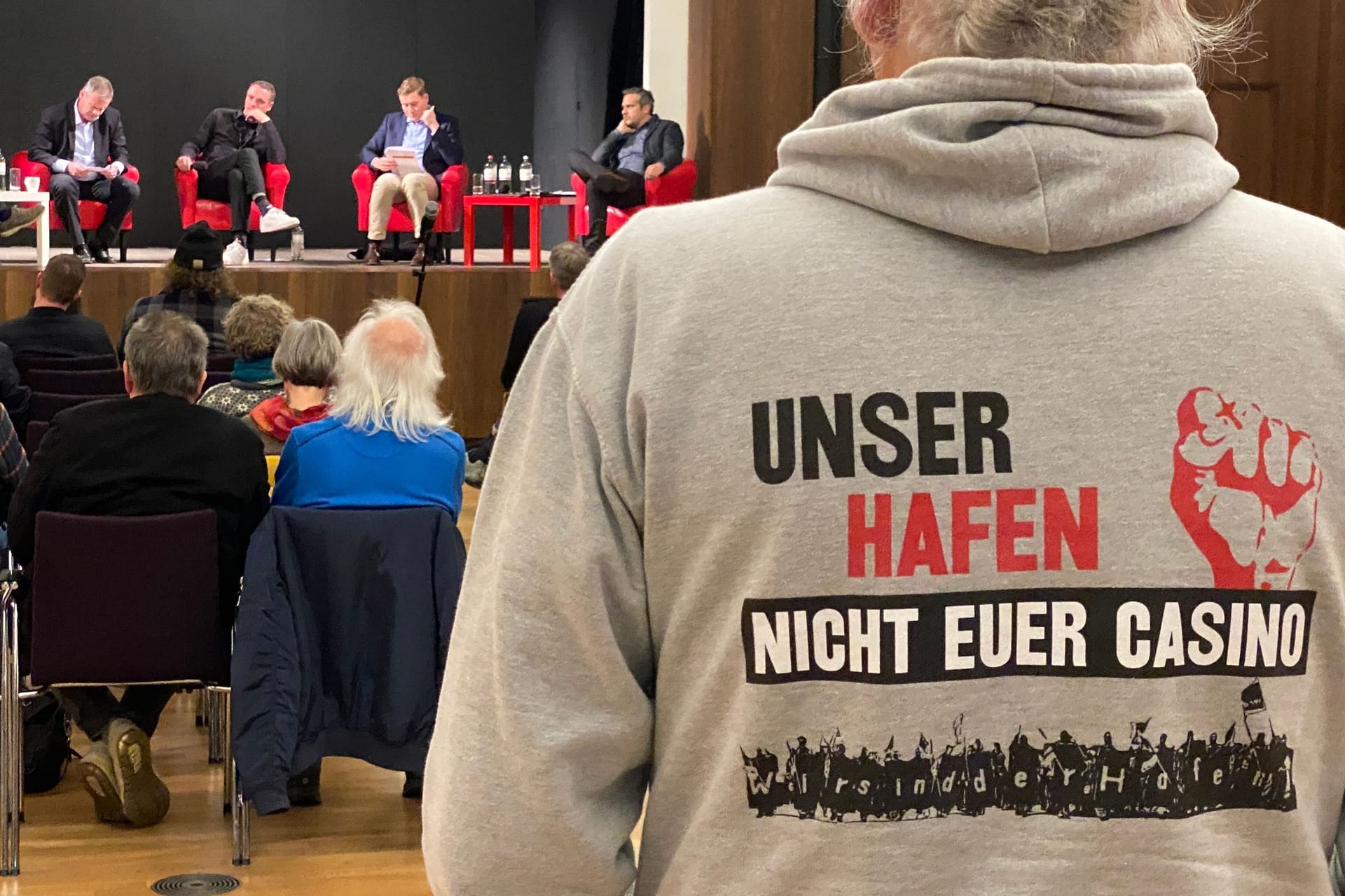 Ein Hafenarbeiter verfolgt die Diskussion: Auf der Rückseite seines Pullis steht "Unser Hafen ist nicht euer Casino".