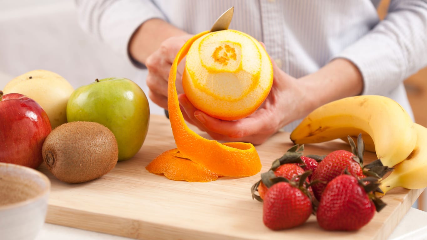 Eine Frau schält eine Orange: Die Schale von Bananen, aber auch von Zitrusfrüchten wie Orangen, ist häufig pestizidbelastet.