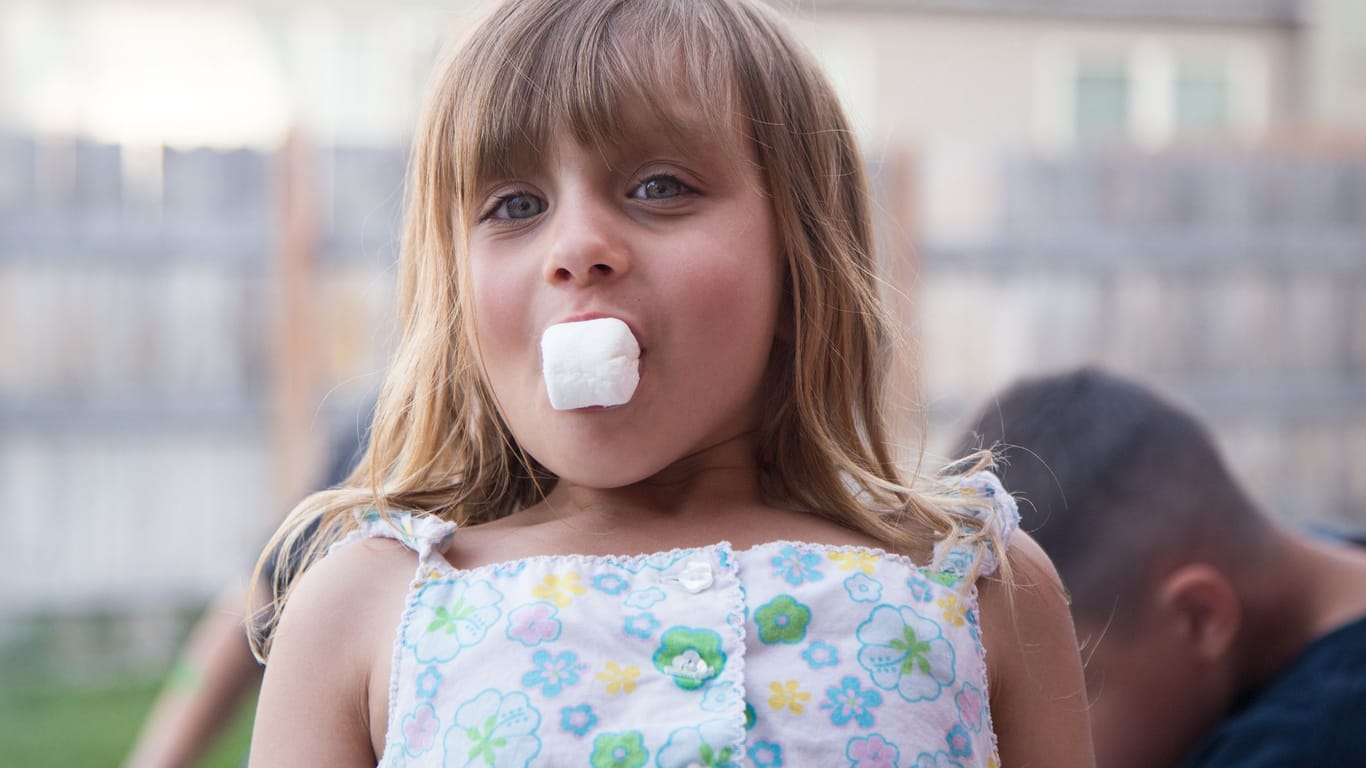 Ein fünfjähriges Mädchen isst einen Marshmallow.