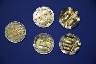 Eine 2-Euro-Münze, die noch gültig und im Umlauf ist (links) im Vergleich mit den mutmaßlich wieder begradigten (Mitte) und endgültig unbrauchbar gemachten Münzen (rechts).