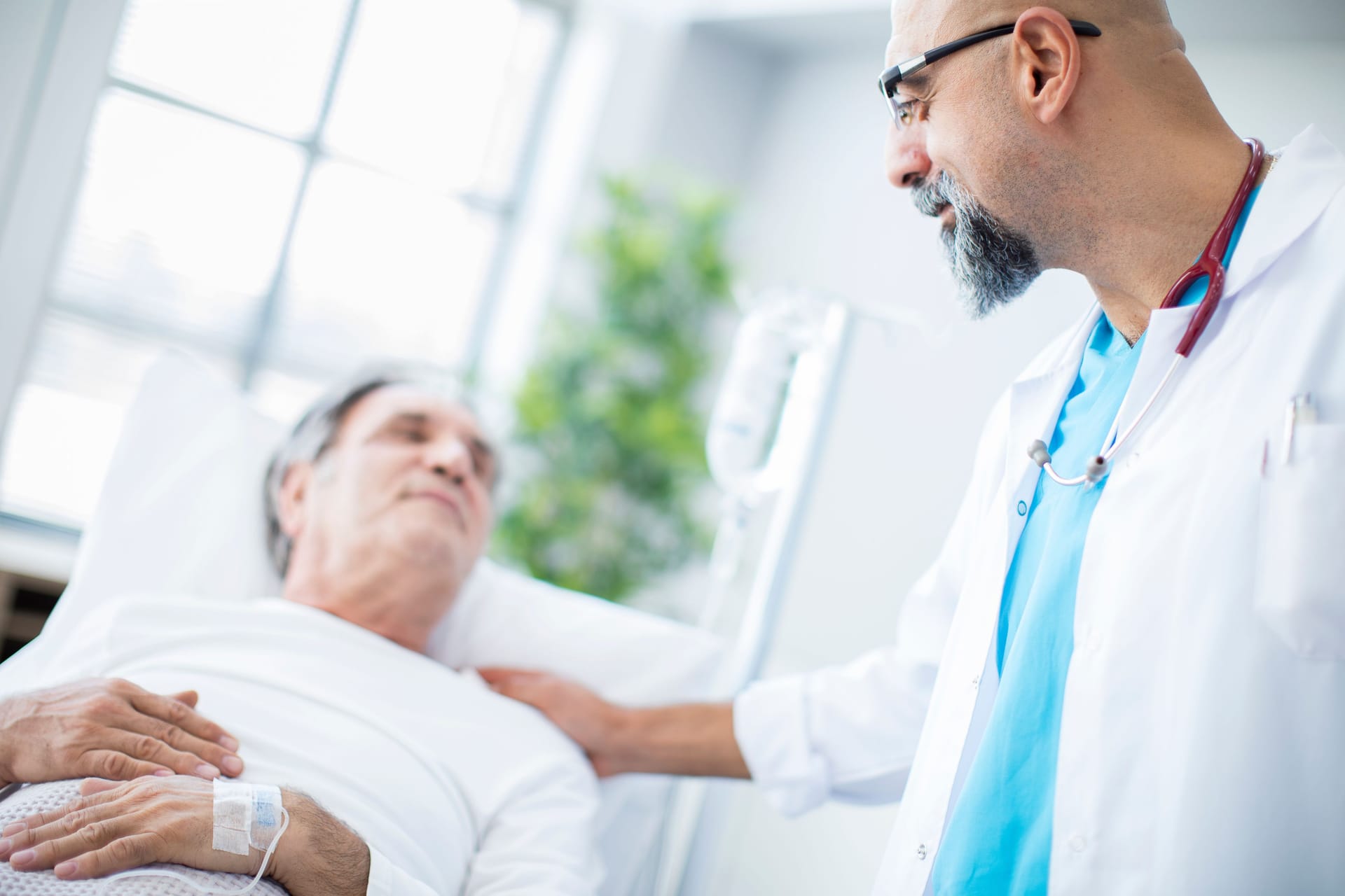 Ein Arzt spricht mit einem im Krankenhausbett liegenden Patienten.