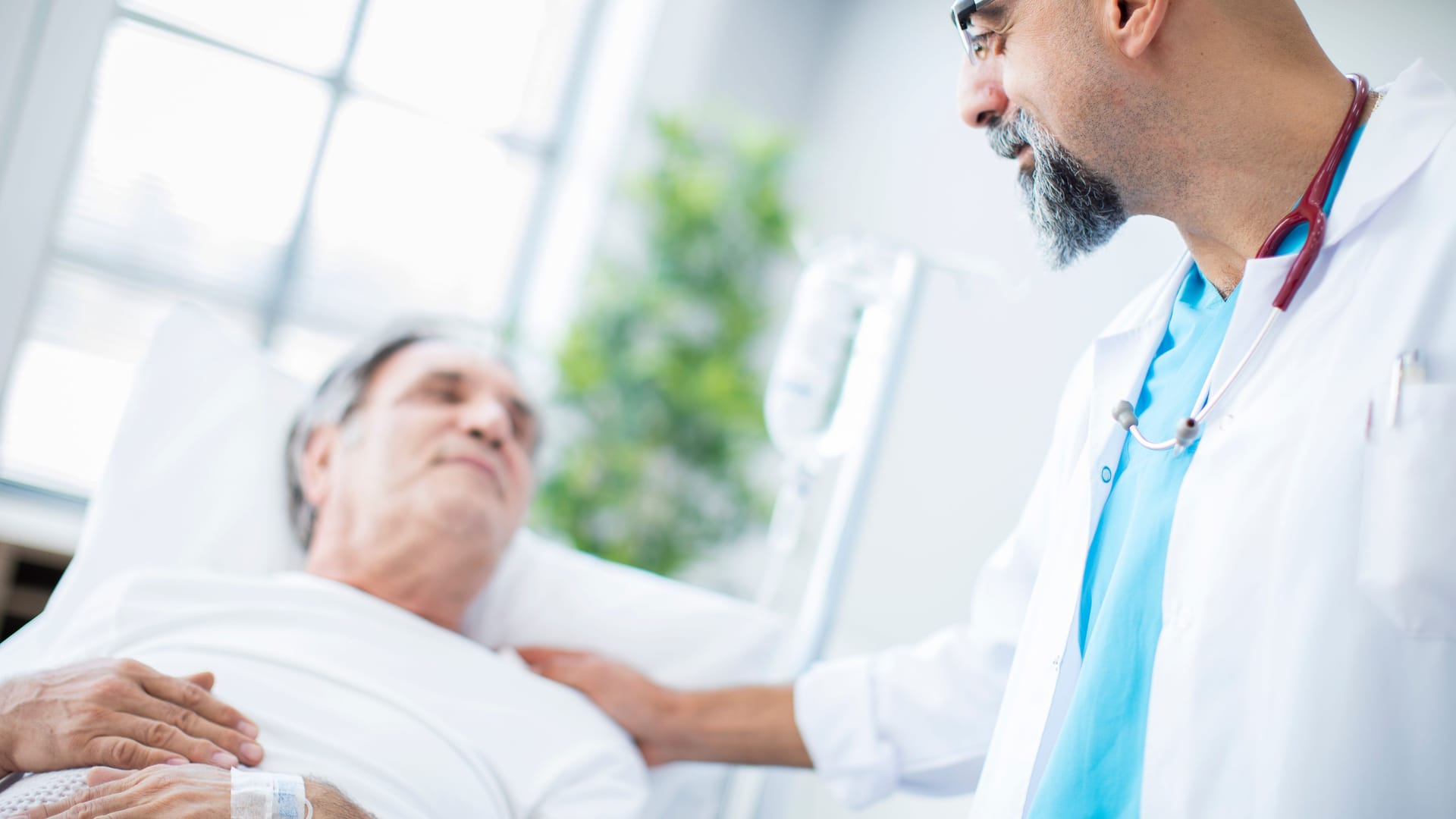 Ein Arzt spricht mit einem im Krankenhausbett liegenden Patienten.