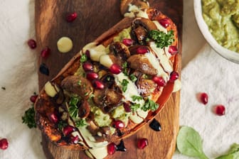 Delicious healthy baked sweet potato with guacamole and mushrooms on a wooden plate on a white table