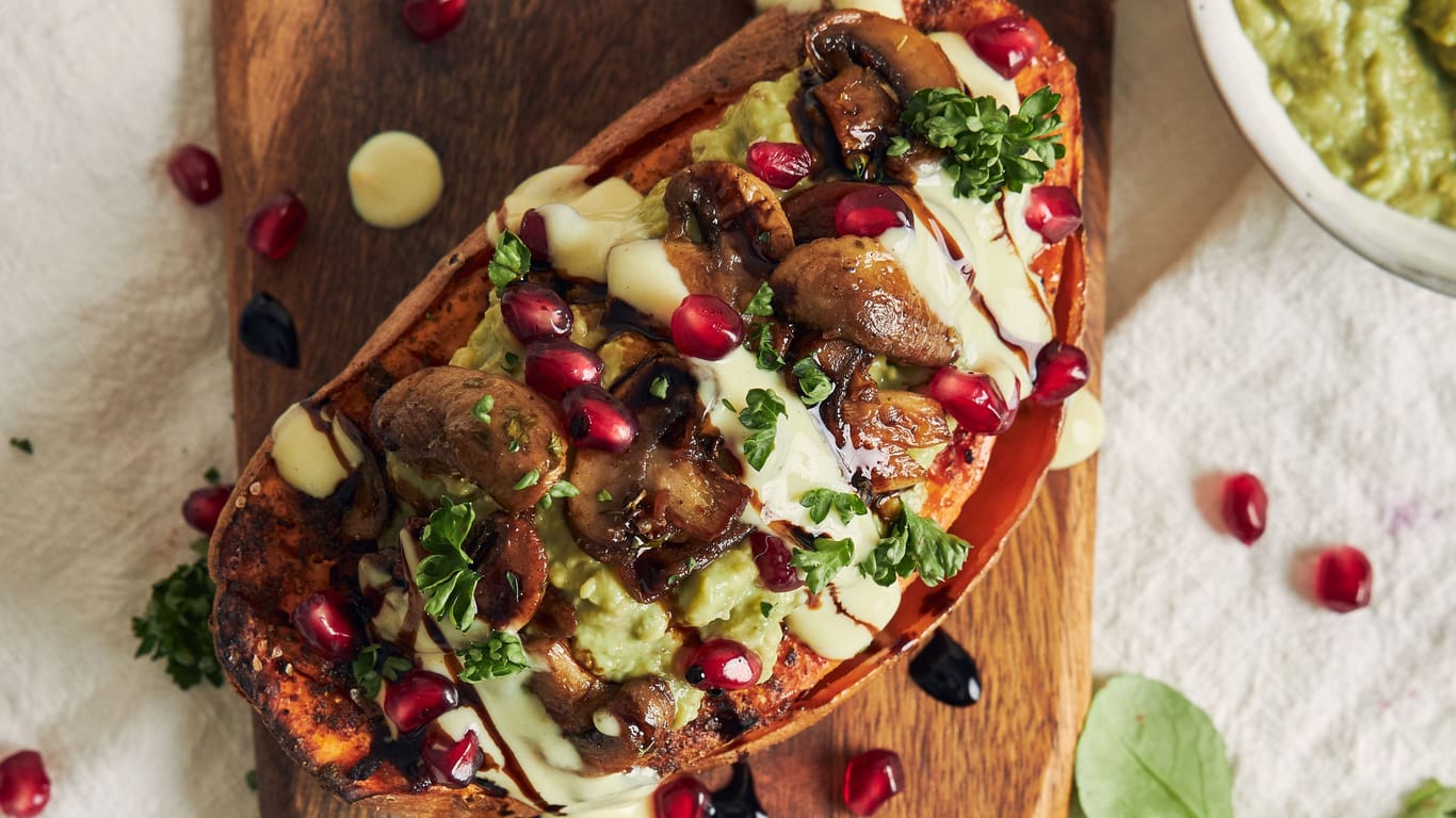 Delicious healthy baked sweet potato with guacamole and mushrooms on a wooden plate on a white table