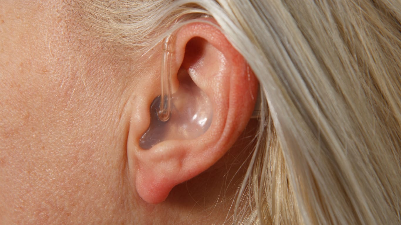 Eine Frau mit Hörgerät (Symbolbild): Nahaufnahme vom Hörgerät im Ohr.