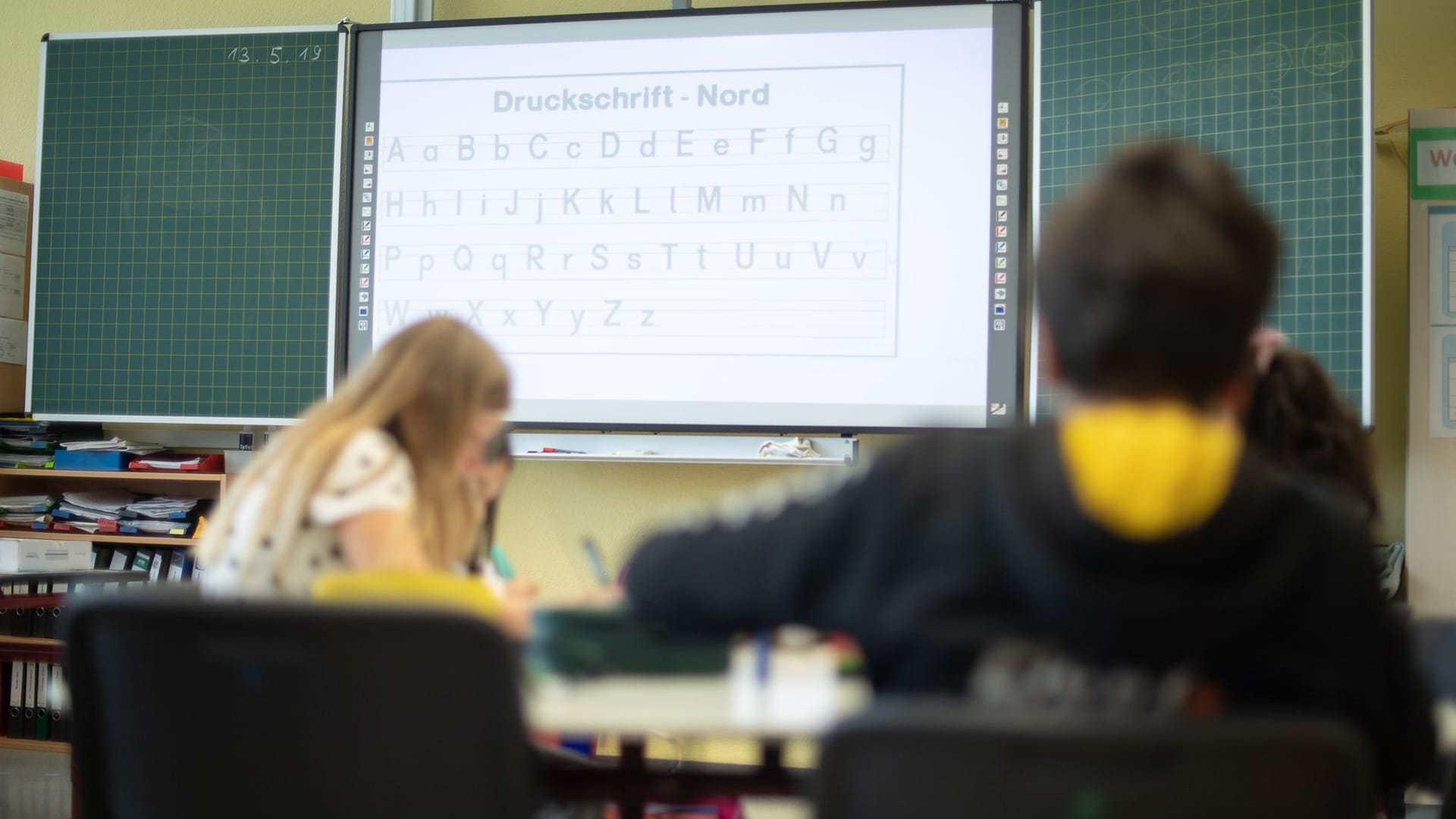 Schüler vor einer Tafel mit digitalem Whiteboard (Symbolbild): Eine Initiative fordert die Rückkehr zu alten Lernmitteln.