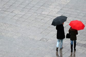 Paar mit rotem und schwarzem Regenschirm (Symbolbild): Es bleibt in weiten Teilen Deutschlands regerisch.