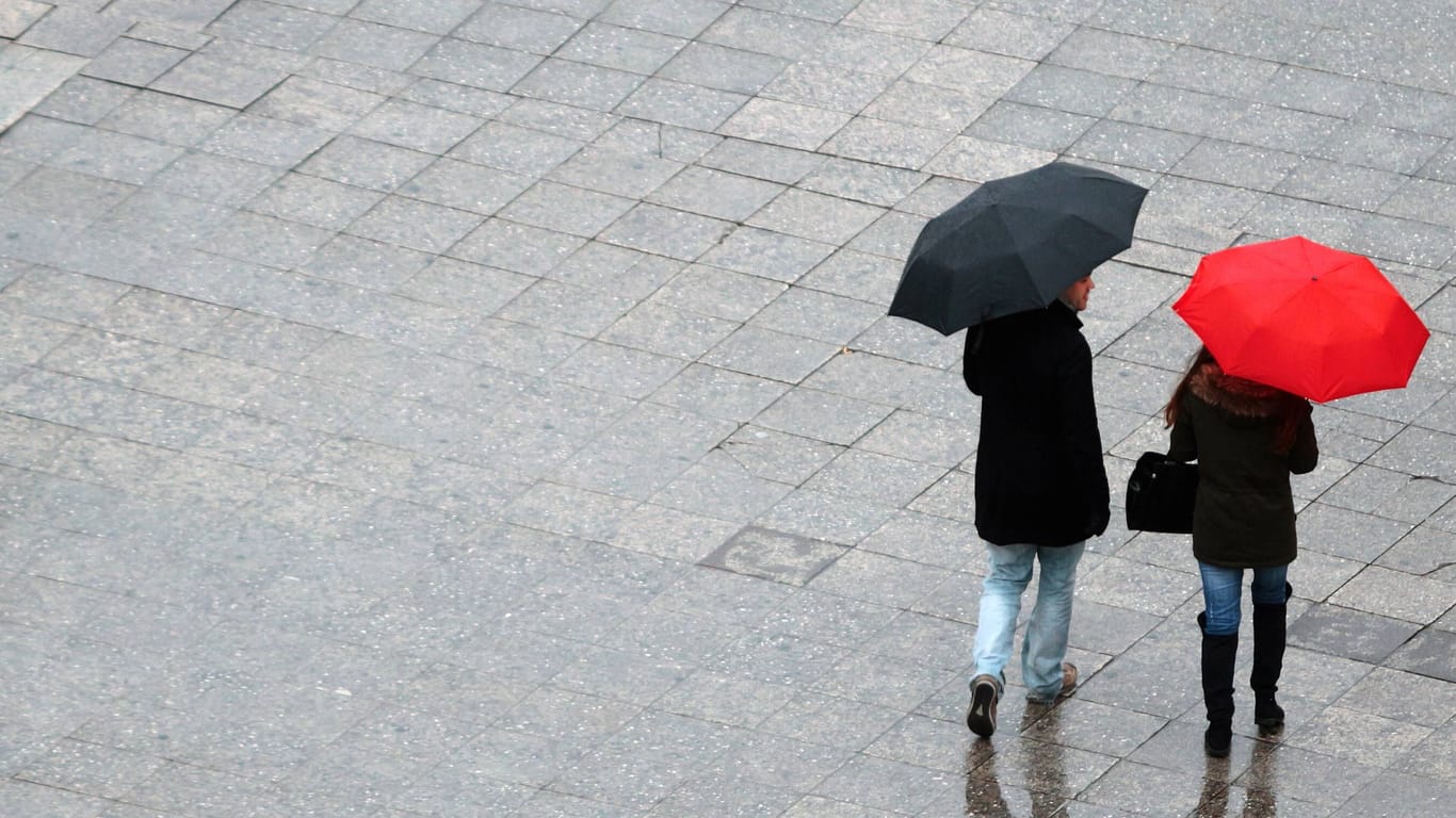 Paar mit rotem und schwarzem Regenschirm (Symbolbild): Es bleibt in weiten Teilen Deutschlands regerisch.