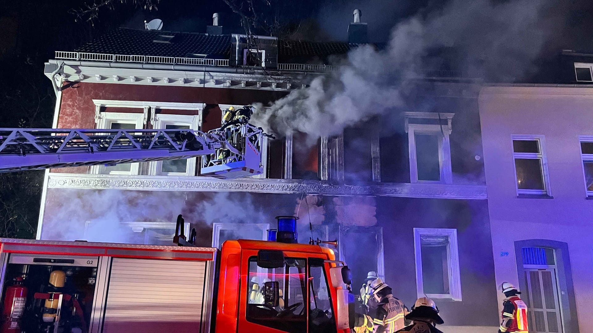 Feuerwehrleute löschen von einer Drehleiter ein Haus.